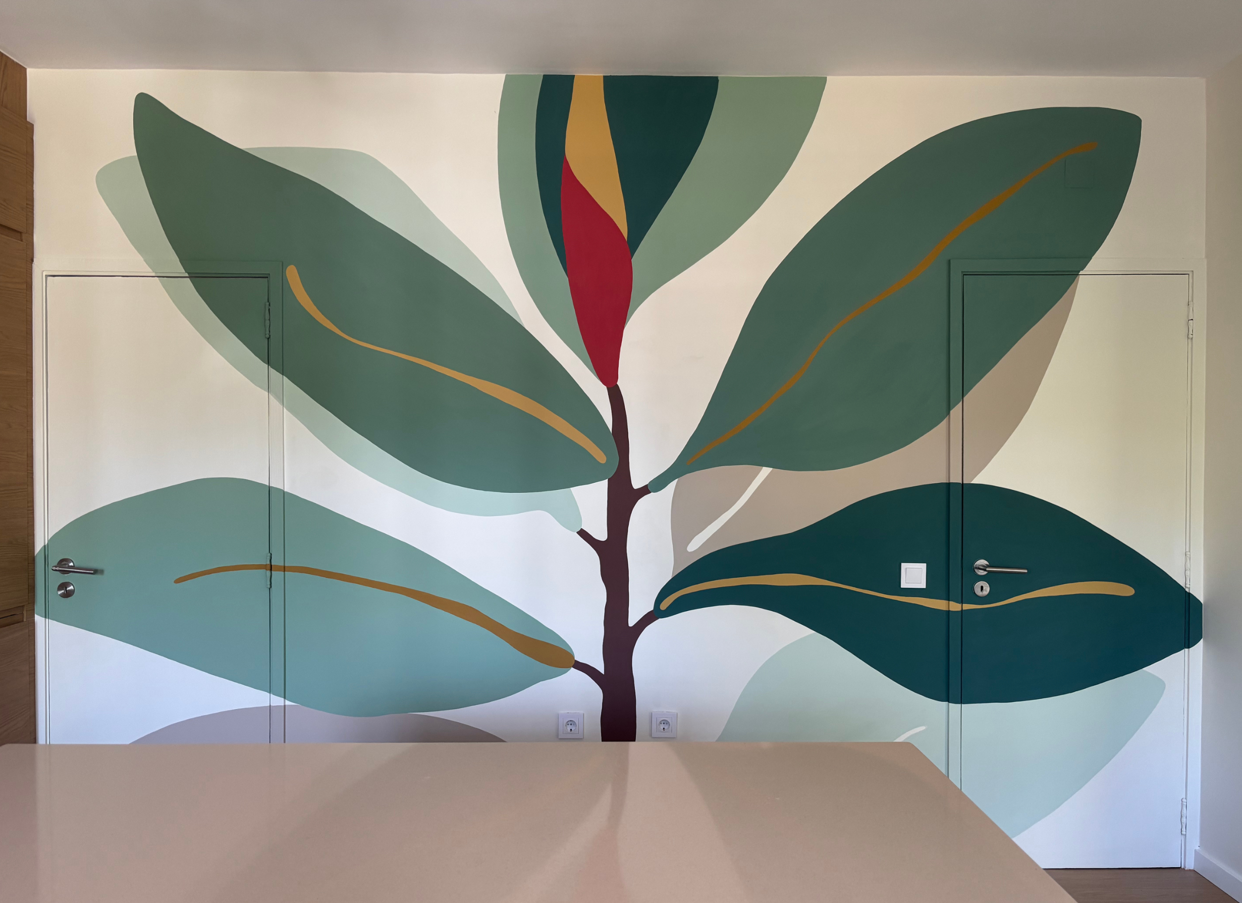 Modern minimalist hand-painted botanical mural in soft green tones on a kitchen wall, complementing warm wood cabinetry and creating a calm natural atmosphere.